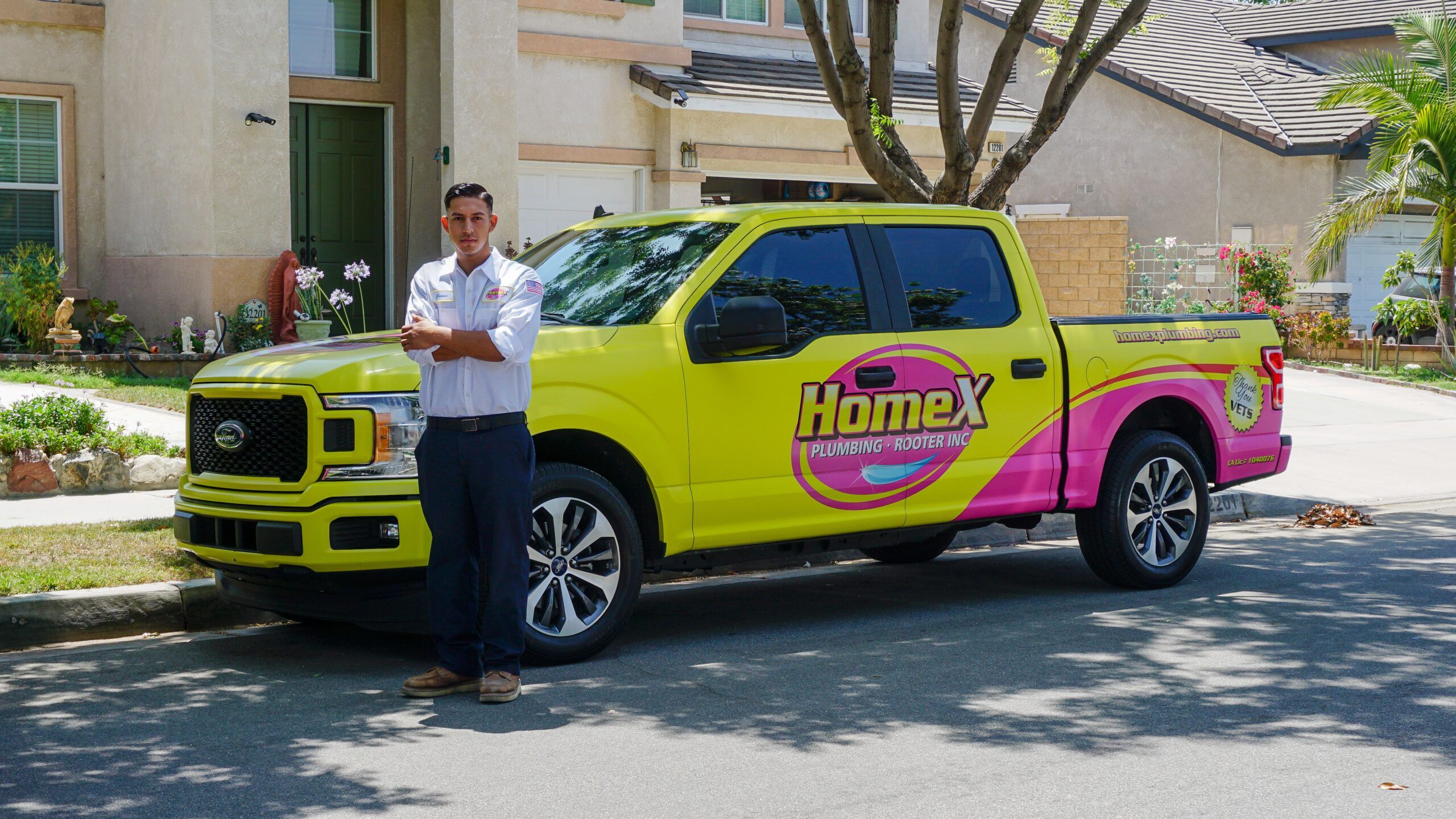 A plumber on the home X team standing next to a company vehicle with yellow and pink colors!