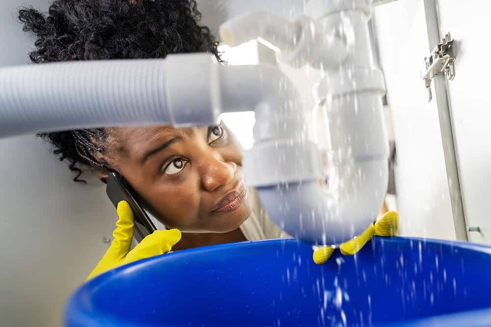 Stressed out customer on the phone with a plumbing service as they watch their drain leak Stressed out customer on the phone with a plumbing service as they watch their drain leak